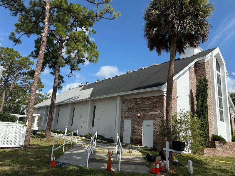 White chapel with a steep new dark shingle roof between tall pines