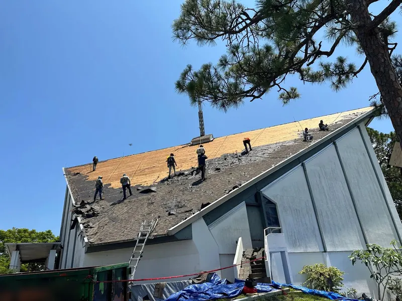 Roofing crew removing old shingles from a steep roof