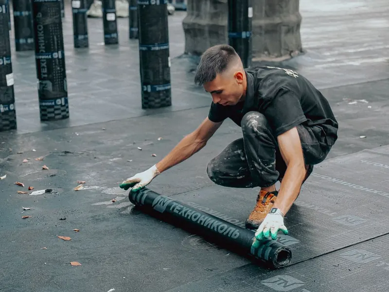 Roofer unrolling a waterproof membrane on a flat commercial roof