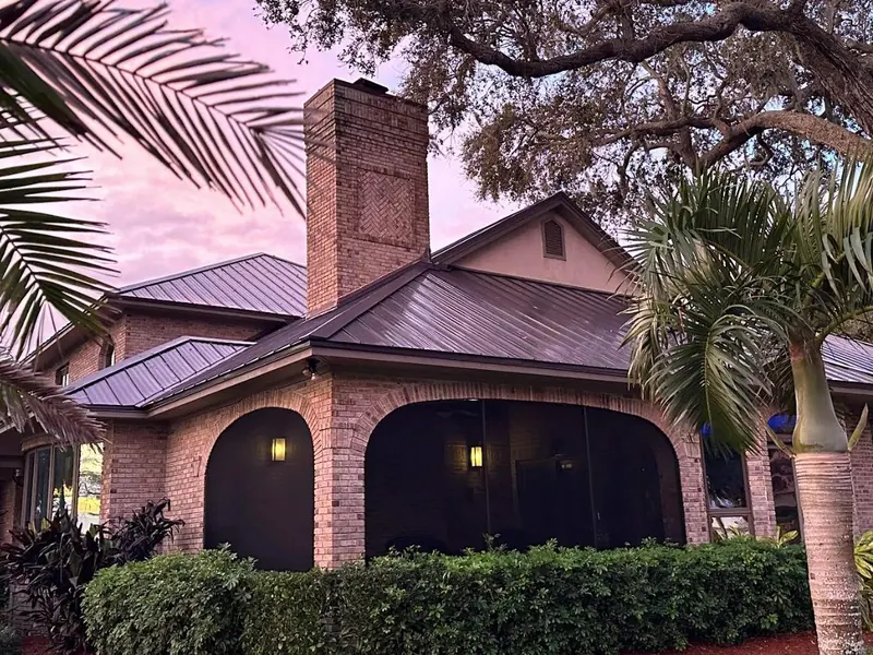 Bronze metal roof over a brick home with arched windows and tropical plants