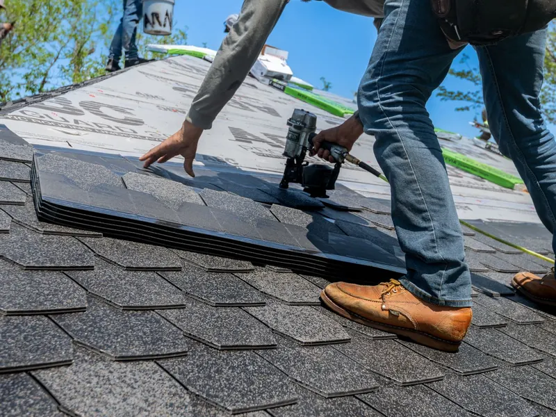 Roofer fixing new grey asphalt shingles with a nail gun