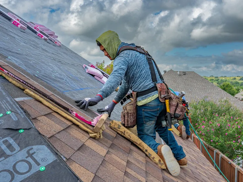 Roofer in a hoodie laying shingles over new underlayment on a sunny day