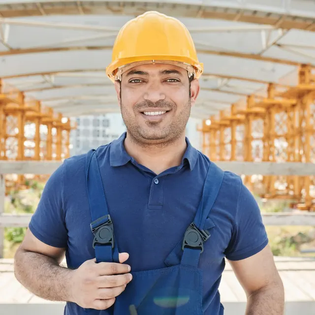 Portrait of a smiling man in a yellow hard hat and work overalls